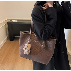 Detail view of leopard print tote bag with brown leather straps and plush bear charm