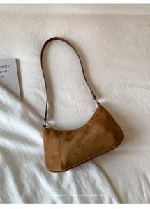 Vue à plat d'un sac sous le bras en daim marron avec fine bandoulière sur fond blanc épuré