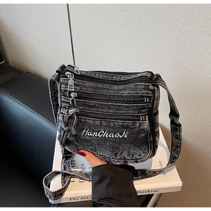 Detail of washed black denim crossbody bag with multiple zippers and white embroidery