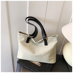 Detail of canvas tote bag with black leather handles and printed logo on the body