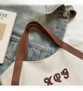 Detail of sturdy brown handles and elegant embroidery on the cream canvas tote bag