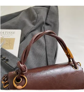 Close-up of dark brown glossy leather handbag featuring braided handles and gold metal rings