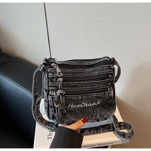 Detail of grey washed denim crossbody bag with multiple zippers and white embroidery
