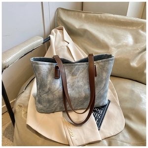 Close-up of light blue denim tote bag with brown leather straps and gold logo detail