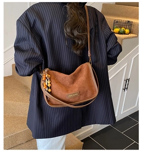 Detail of a brown matte leather crossbody bag with ethnic wooden bead charm accessory