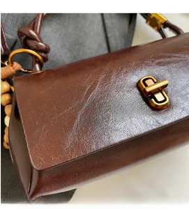 Detail of vintage brown leather bag with twisted handle and gold clasp on suit fabric