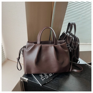 Detail of dark brown leather tote bag with cloud pleats on a minimalist wooden surface
