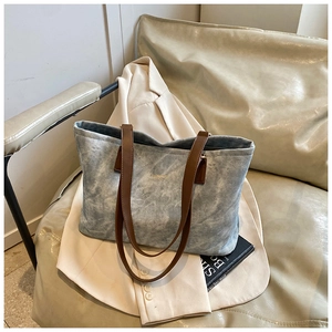 Detail of blue textured tote bag with brown leather straps on an ivory blazer