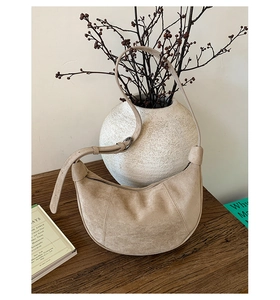 Dettaglio della borsa a tracolla a mezzaluna beige con cinturino su scrivania vintage