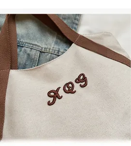 Detailed close-up of canvas tote with brown embroidered letters and woven strap