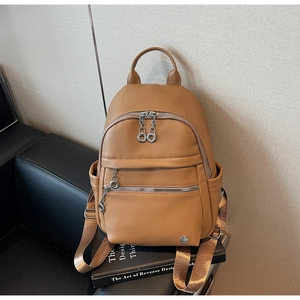Close-up of camel lychee pattern leather backpack with silver zippers on a black sofa