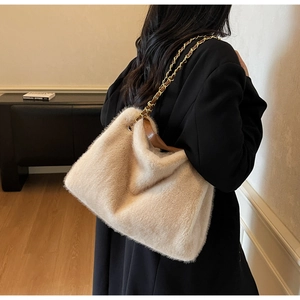 Detail view of the beige plush tote bag with gold chain strap on a black blazer