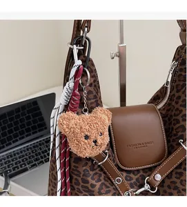 Close-up of a plush brown bear keychain hanging on a leopard print tote bag with metal chain