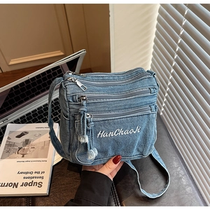 Detail view of denim crossbody bag with multiple zippers and embroidered logo text