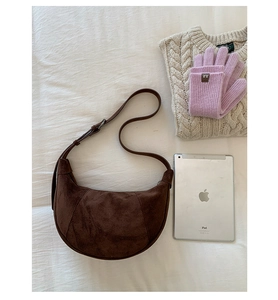 Top view of dark brown suede crescent bag with adjustable strap and lifestyle props