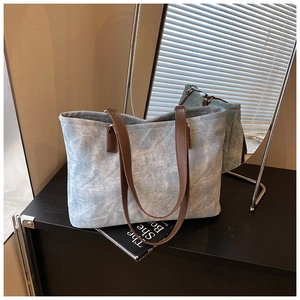 Detail of blue denim tote bag with brown leather handles and gold lettering
