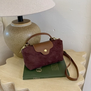 Detail of burgundy faux suede handbag with brown litchi leather strap and gold hardware