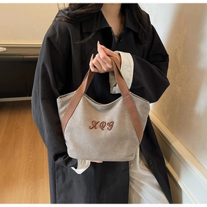 Close-up of canvas tote bag featuring brown XQG embroidered logo and webbing handles