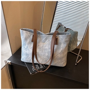 Close-up of light blue canvas tote bag featuring brown leather handles and gold metal hardware