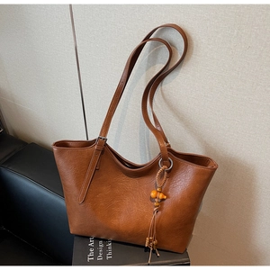 Brown tote bag with double straps and tassel charm on a decorative book base