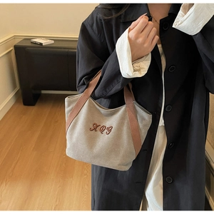 Detail of canvas tote bag with brown woven handles held by woman in black coat