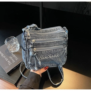 Detail of blue denim crossbody bag with multiple zippers and Han Chao Ji embroidery