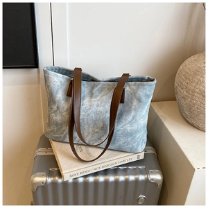 Close-up of light blue washed canvas tote bag with brown leather handles and gold text