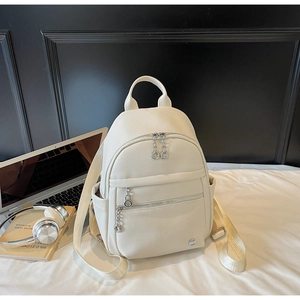 Close-up of white pebble leather backpack with metal zippers on a minimalist bed set