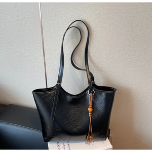 Detail of black wrinkled texture tote bag with brown wooden bead tassel on white books