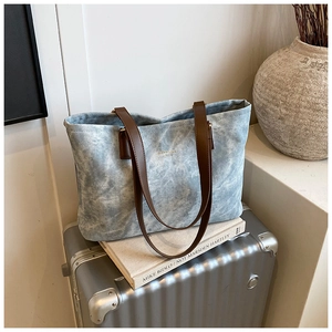Detail of blue tie-dye canvas tote bag with brown leather handles on minimalist backdrop