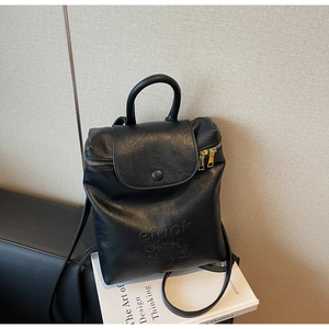 Détail du sac à dos en cuir mat noir avec texte gaufré sur fond minimaliste beige