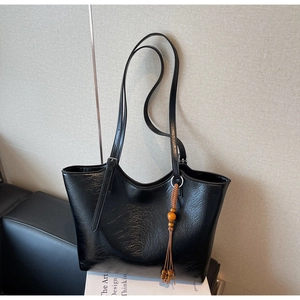 Detail of black tote bag with glossy wrinkled texture and wooden bead tassel decoration