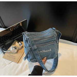 Detailed shot of a blue denim crossbody bag featuring multiple zippers and white embroidery