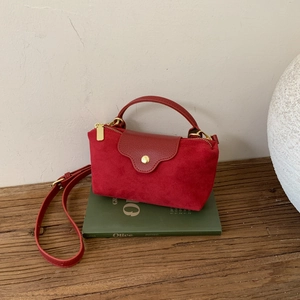 Detail view of mini red suede bag on green book with gold zipper and leather strap