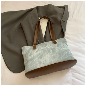 Close-up of a blue washed canvas tote bag with brown leather handles on a white background