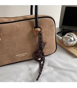 Brown suede tote bag detail featuring a woven rope knot charm and brand logo side print