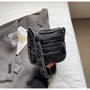 Detail of dark denim crossbody bag featuring multi-zipper pockets and brand embroidery