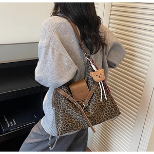 Detail of leopard print tote bag with brown leather straps and a plush bear charm