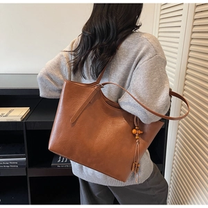 Brown leather tote bag featuring a wooden bead tassel and textured PU surface