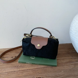 Detail of suede crossbody bag with leather flap on vintage book and wooden surface