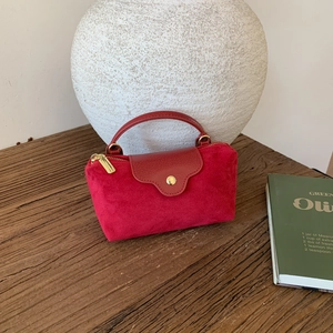 Close-up of red suede and pebble leather handbag with gold zipper and metal buckle detail