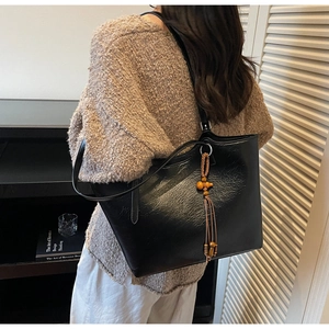 Detail of black faux leather tote bag with wooden bead and brown tassel accent on model