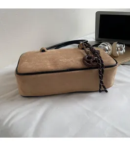 Close-up of brown suede bag featuring black trim and decorative pretzel-shaped knot charm