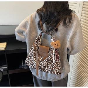 Detail of leopard print tote bag featuring a plush bear charm and chain shoulder strap