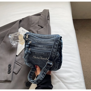 Detail of blue denim crossbody bag with multiple zipper pockets and adjustable strap