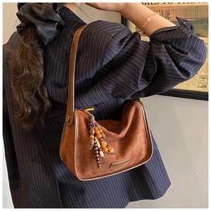 Detail of a brown matte shoulder bag featuring colorful wooden bead charm and gold logo plate