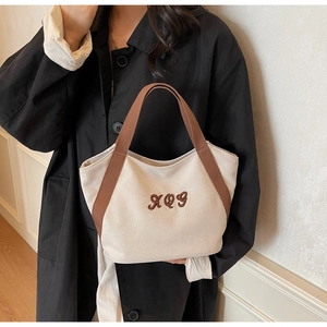 Detail of canvas tote bag featuring brown embroidered letters and durable woven handles