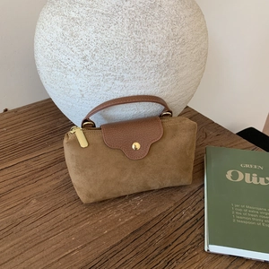 Detail of suede handbag with contrast leather lid and gold buckle on a rustic wooden desk