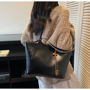 Detail of black faux leather tote bag with vintage texture and wooden bead tassel accessory