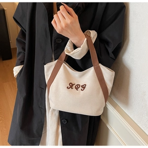 Close-up of the beige canvas tote bag featuring brown XQG embroidery and sturdy handles